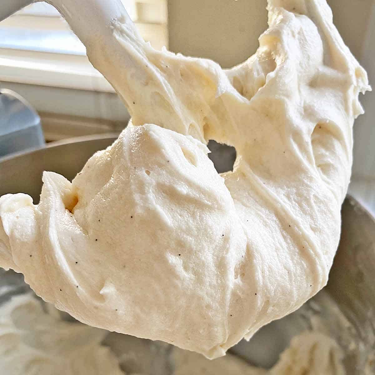 The beater attachment of an electric mixer lifted up and covered with homemade vanilla bean buttercream frosting.