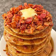 A tall stack of nine bacon pancakes with maple syrup and butter.