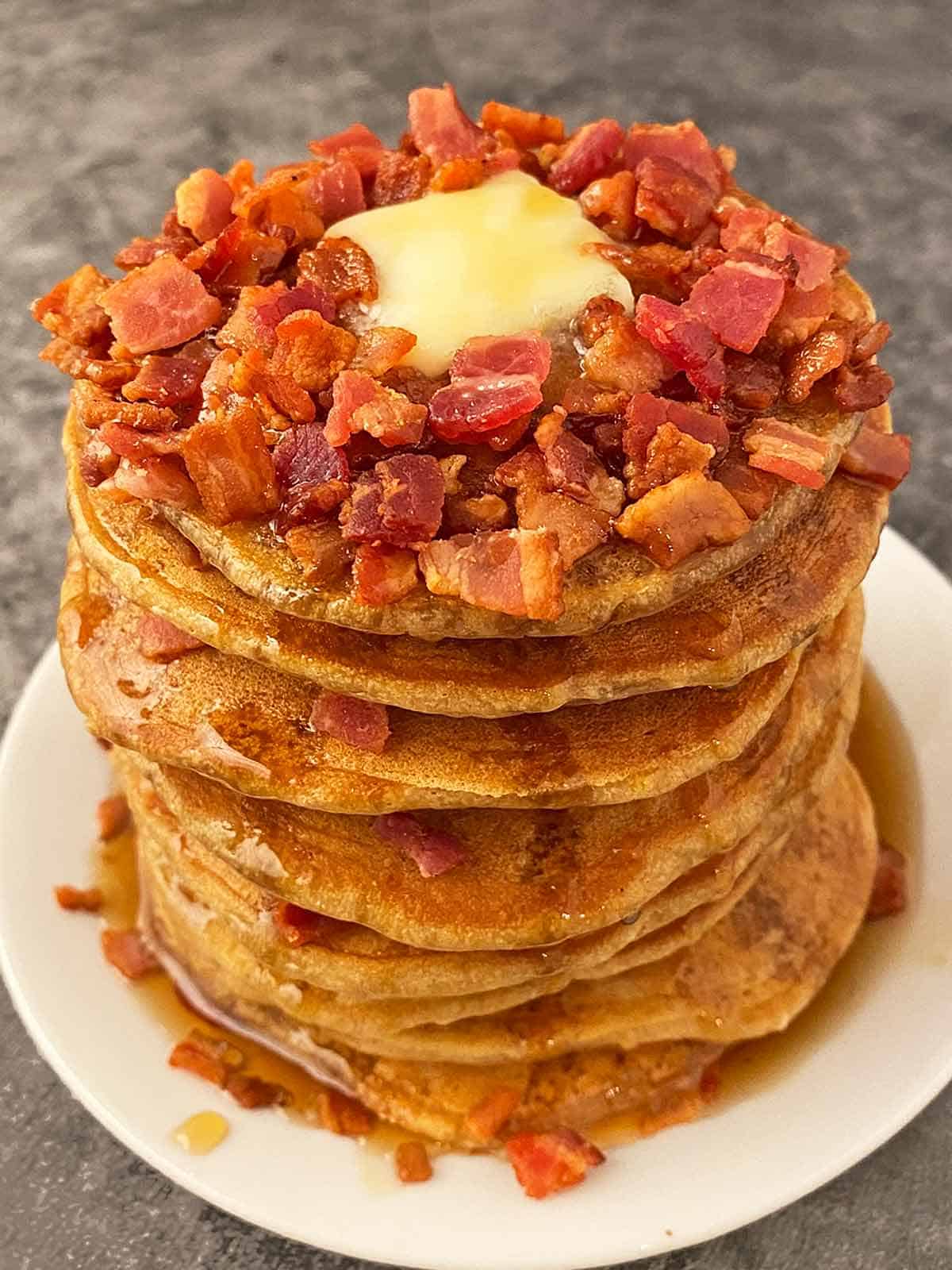 A tall stack of nine bacon pancakes with maple syrup and butter.