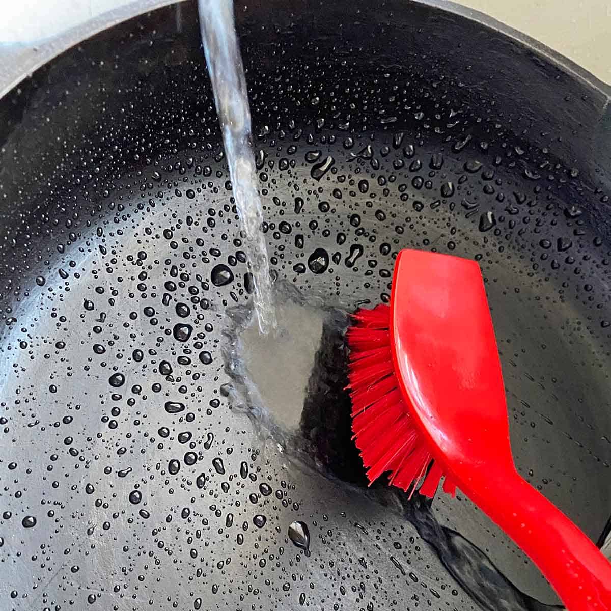washing a cast iron pan with water and a stiff brush.