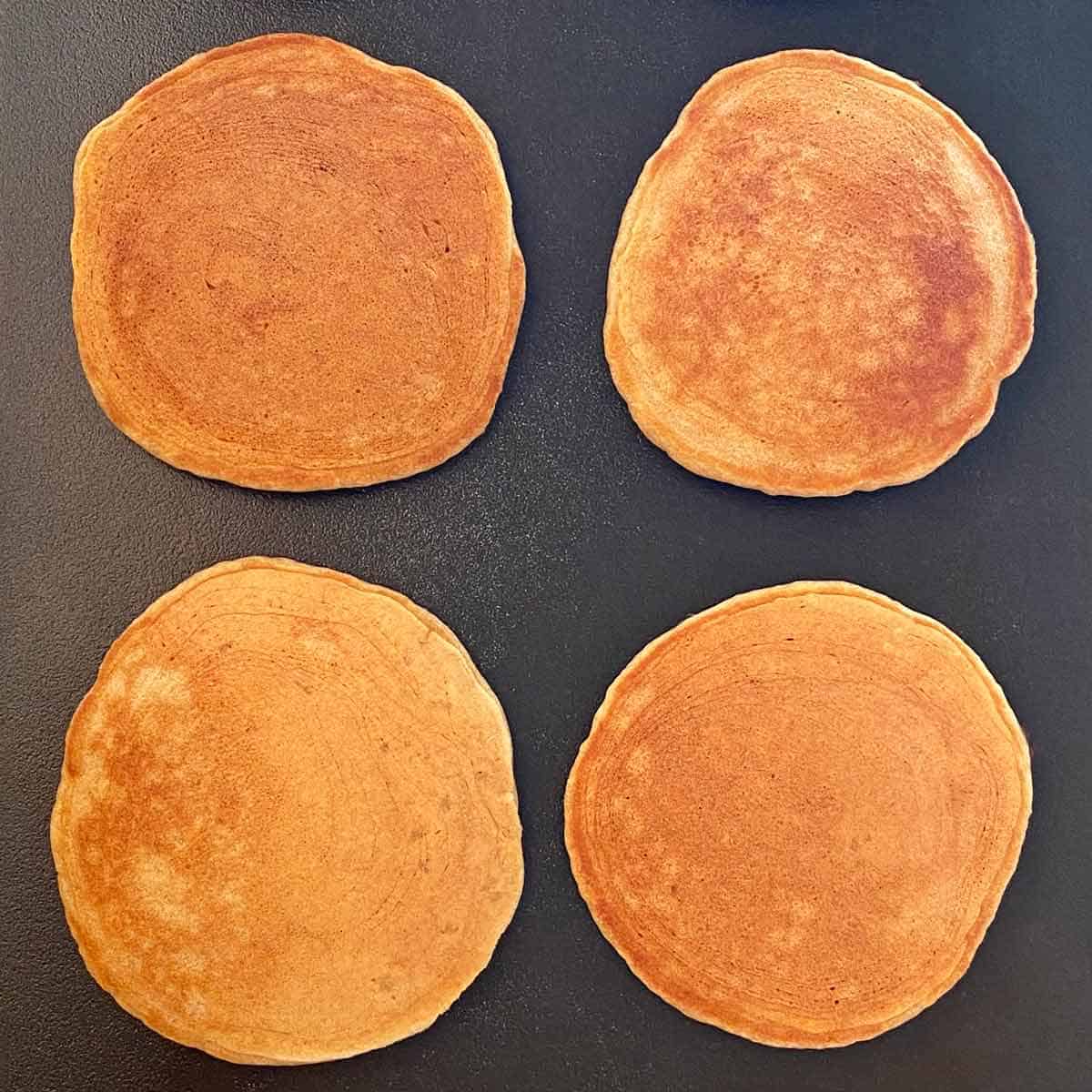 Four golden brown pancakes on a griddle.