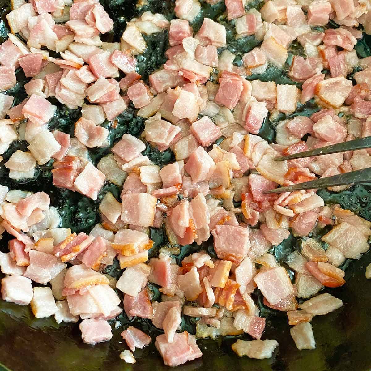 Cooking chopped sliced bacon in a hot skillet with a fork.