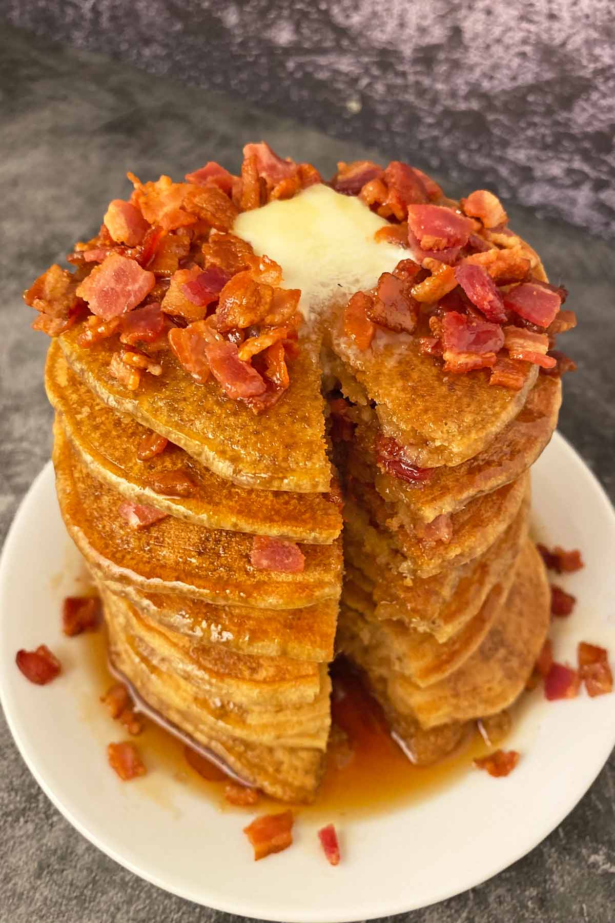 A stack of bacon pancakes drizzled with maple syrup, with a bite cut out.