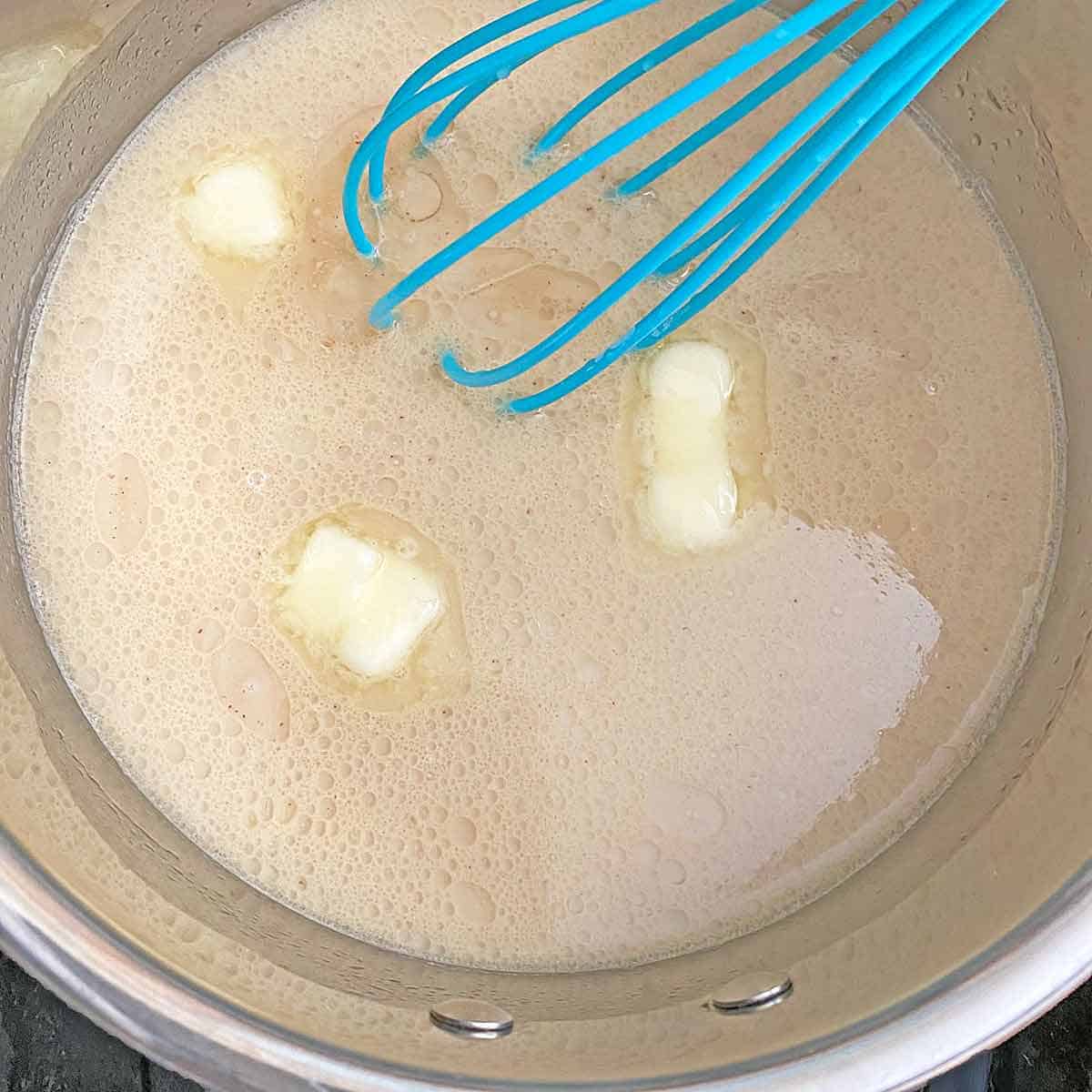 Whisking butter into the warm milk mixture in a saucepan.