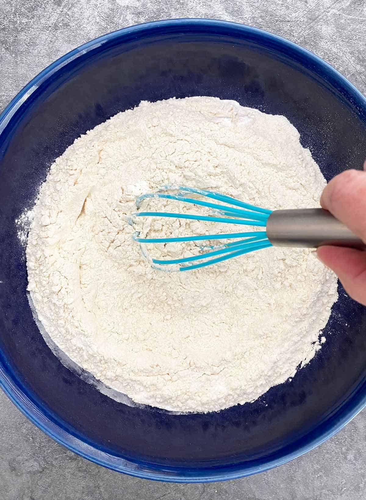 Whisking together flour, sugar, salt and baking powder in a blue bowl to combine.