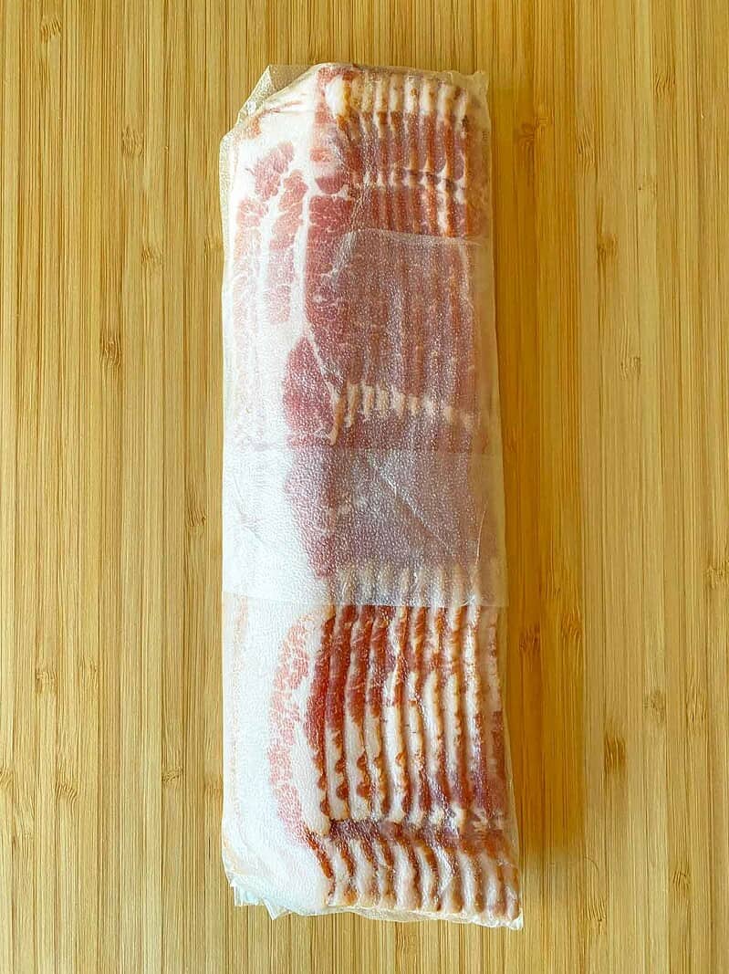 One half pound of bacon tightly wrapped in Press N Seal plastic wrap, on a cutting board.