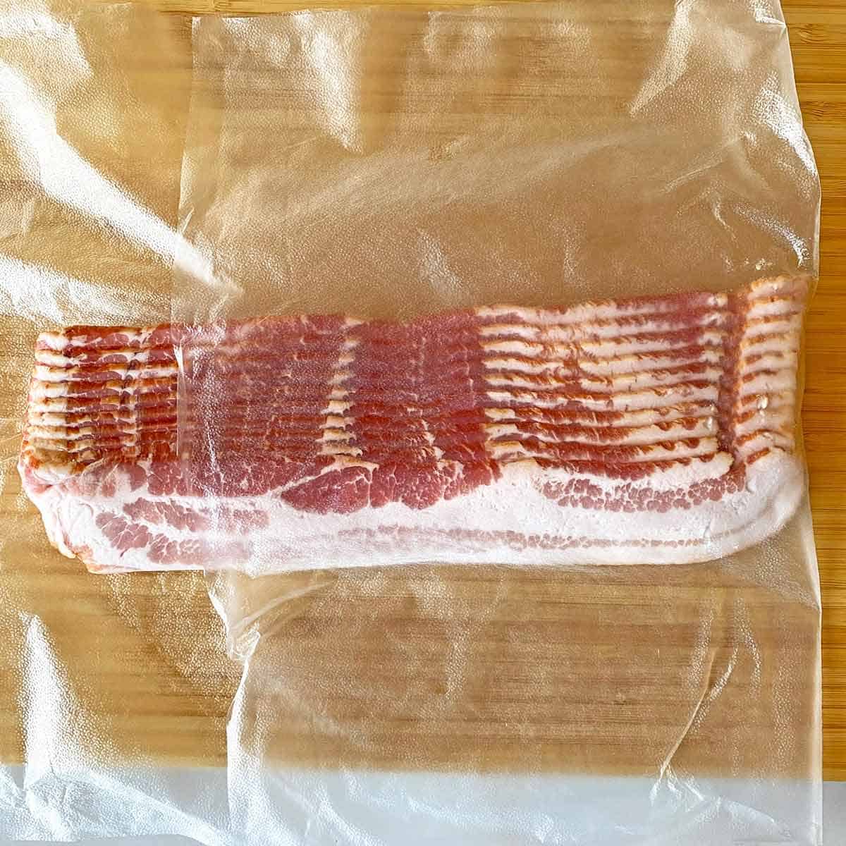 Wrapping a half pound of raw bacon slices in a sheet of plastic wrap.