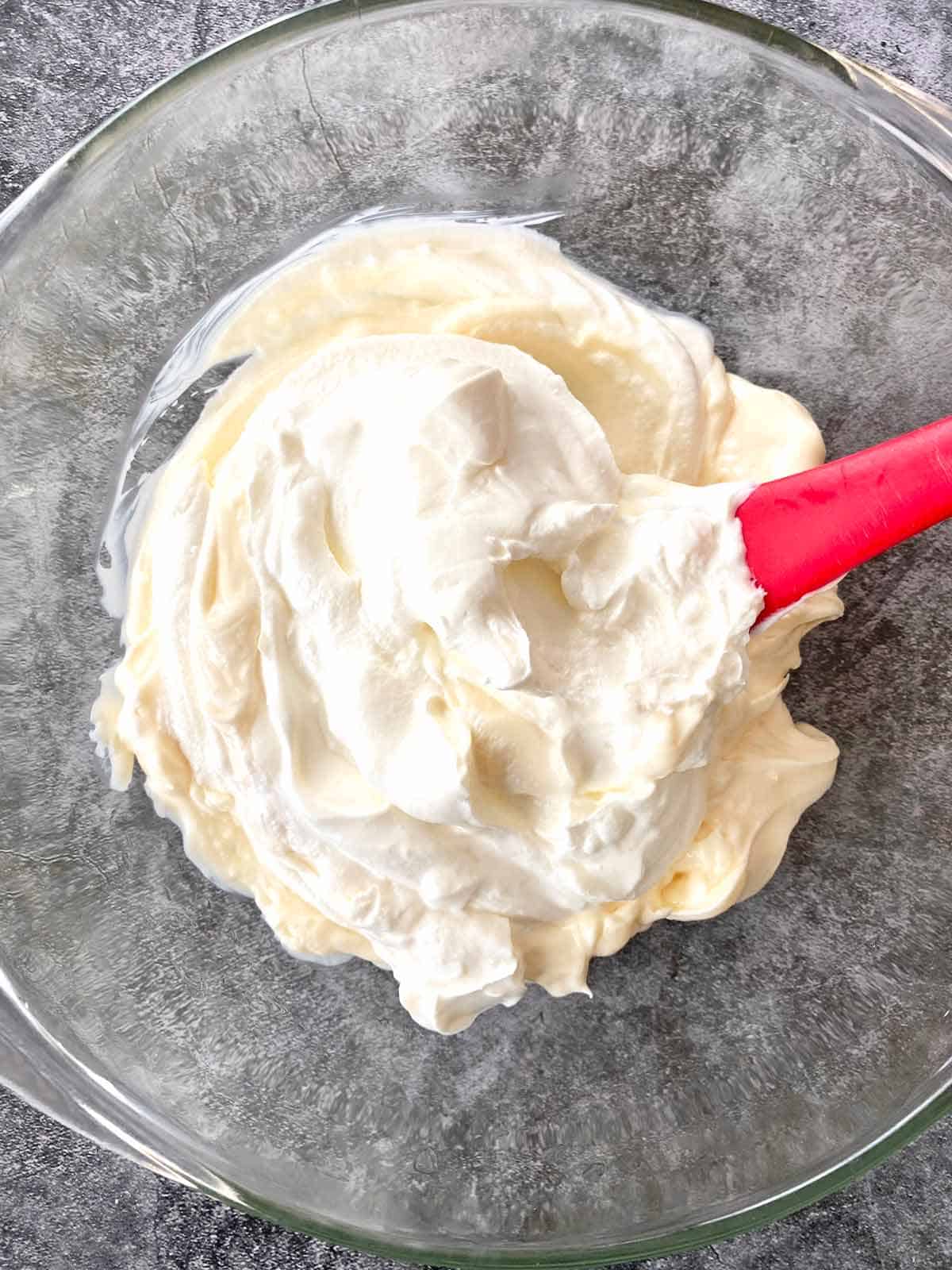 Combining sour cream and mayonnaise in a glass bowl.