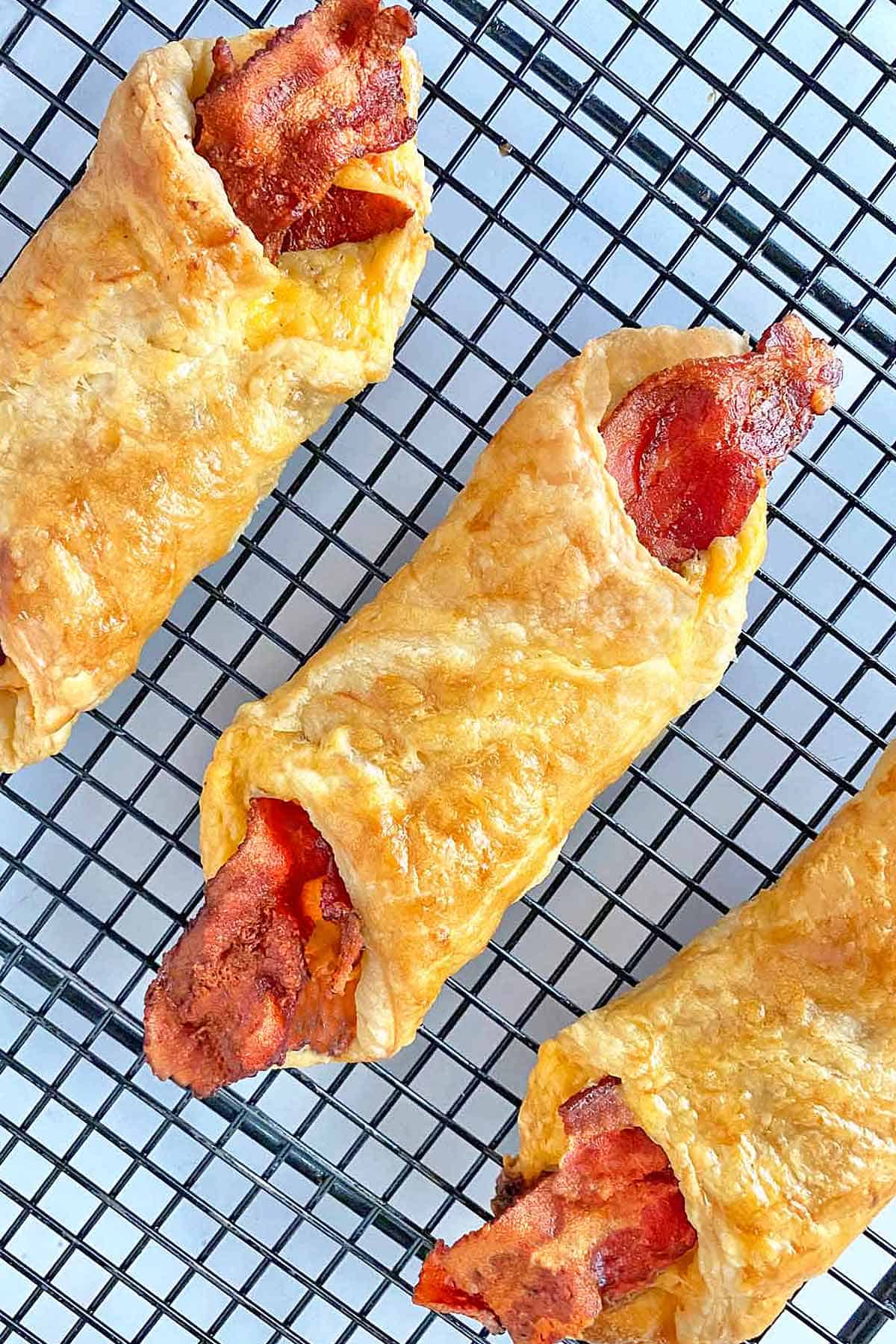 Three freshly baked bacon and cheese turnovers on a cooling rack.