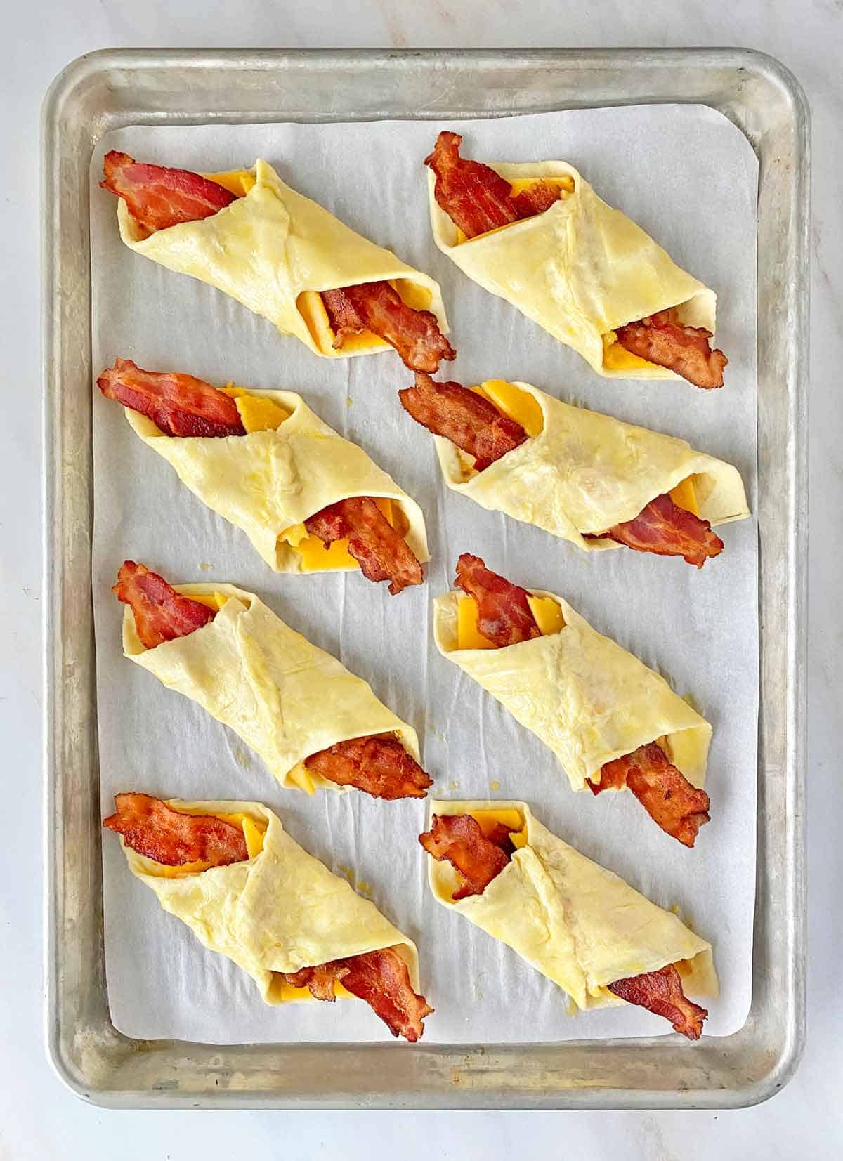 Unbaked cheese bacon turnovers on a cookie sheet.