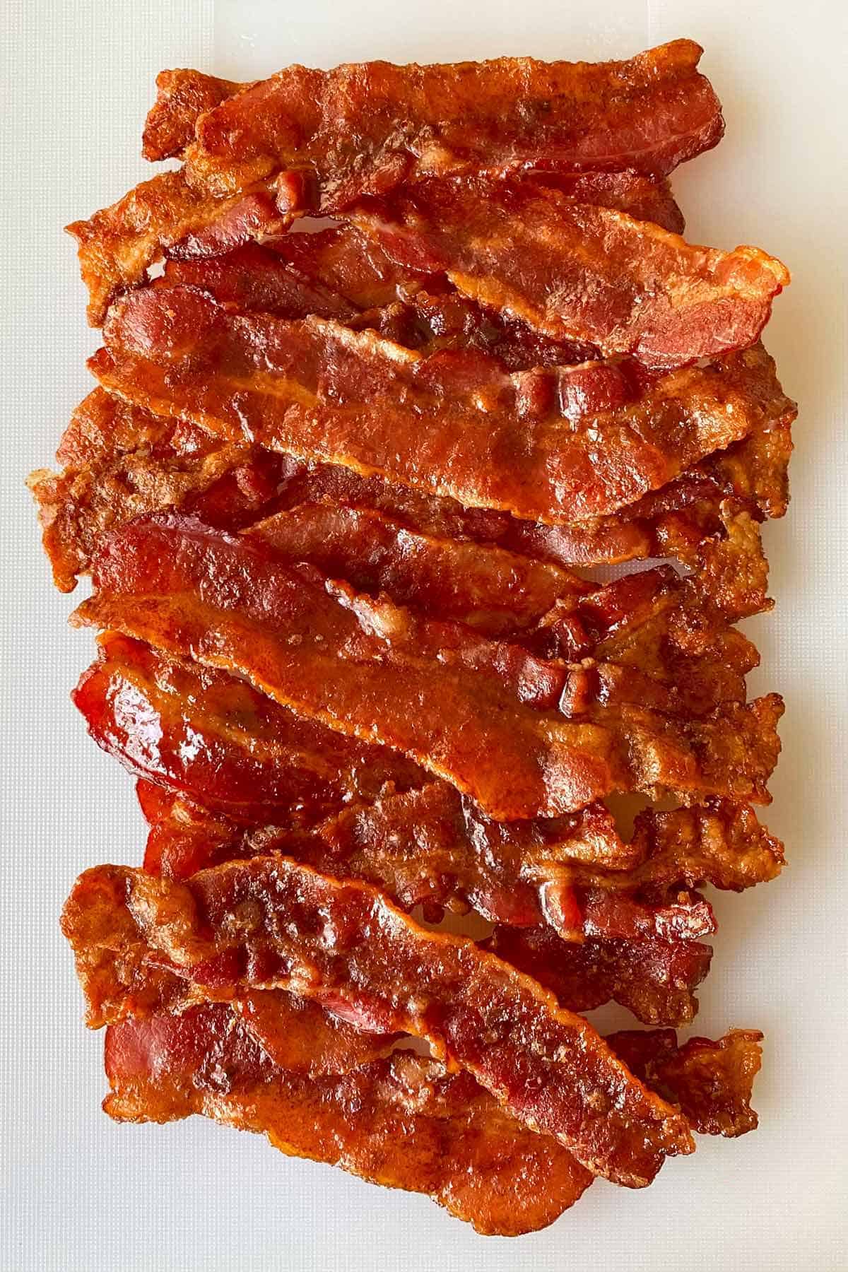 Cooked cracked bacon arranged on a white cutting board.