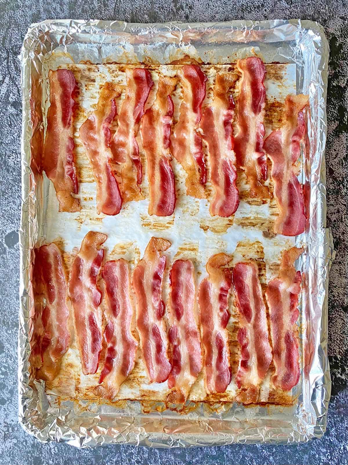 Partially cooked bacon strips on a baking pan.