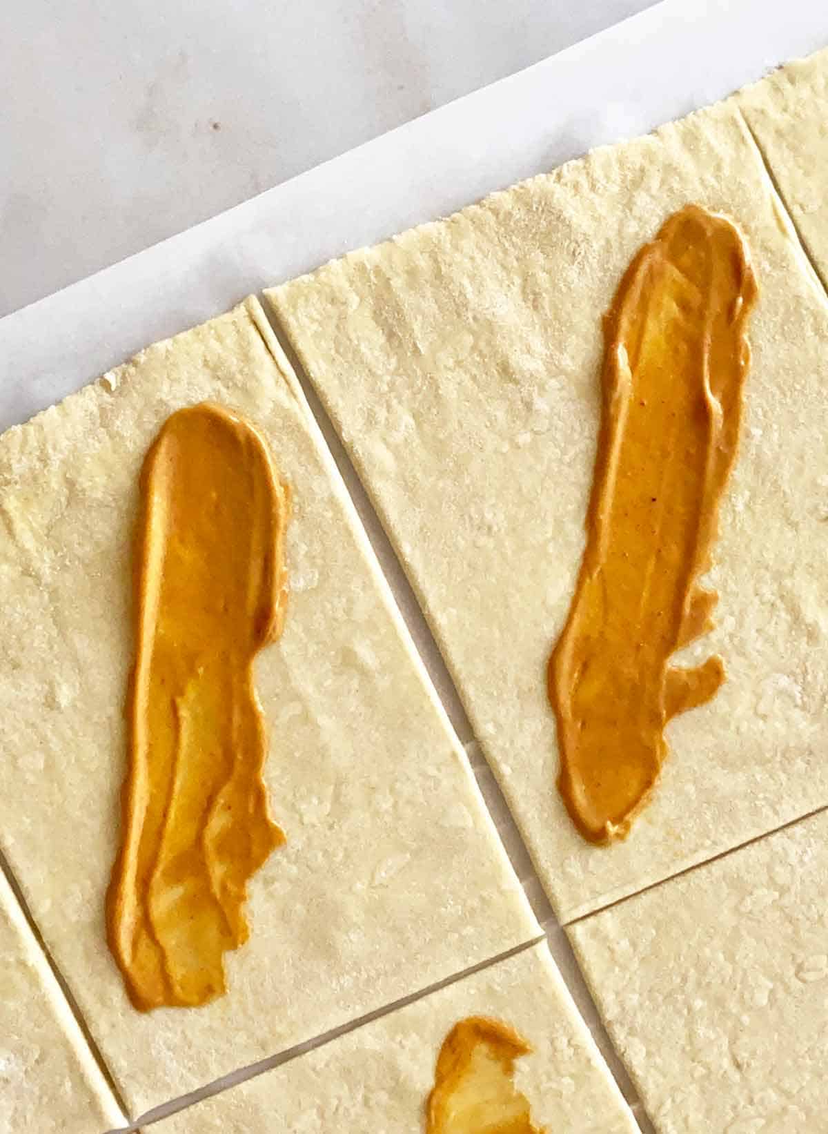 Spreading spicy mustard on puff pastry rectangles.