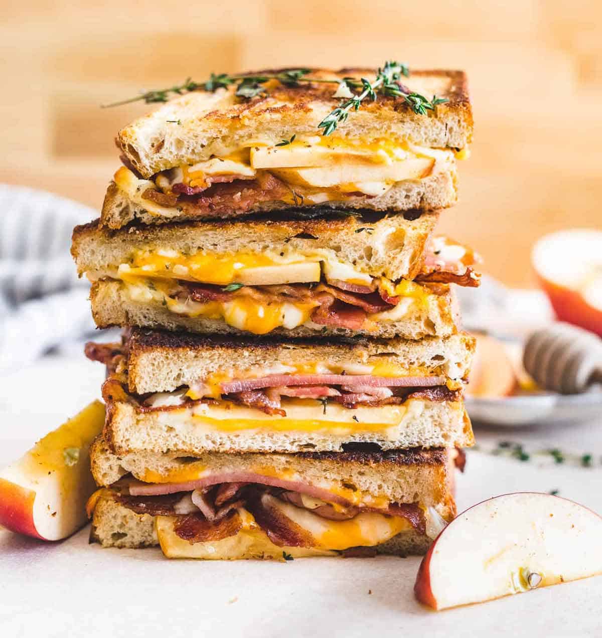 Two apple bacon cheddar sandwiches stacked on a cutting board.