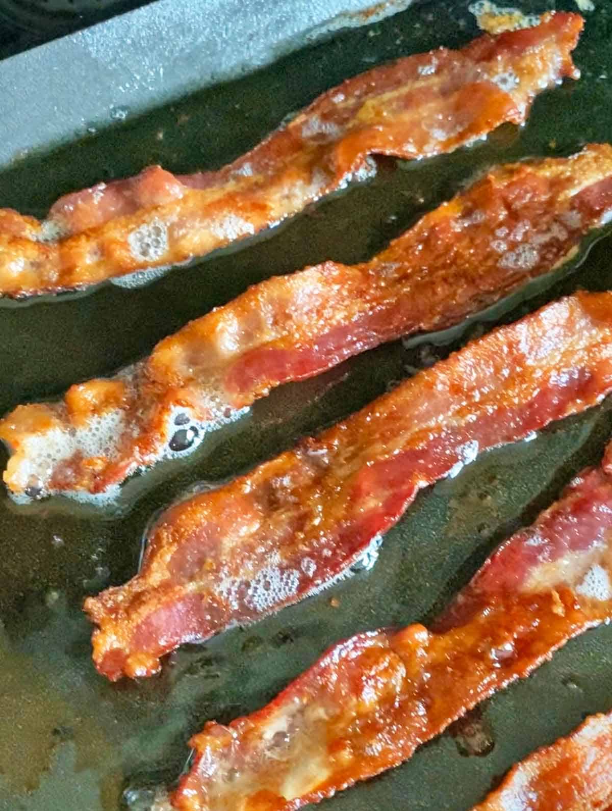 Five crispy bacon slices cooked in a square cast iron pan.