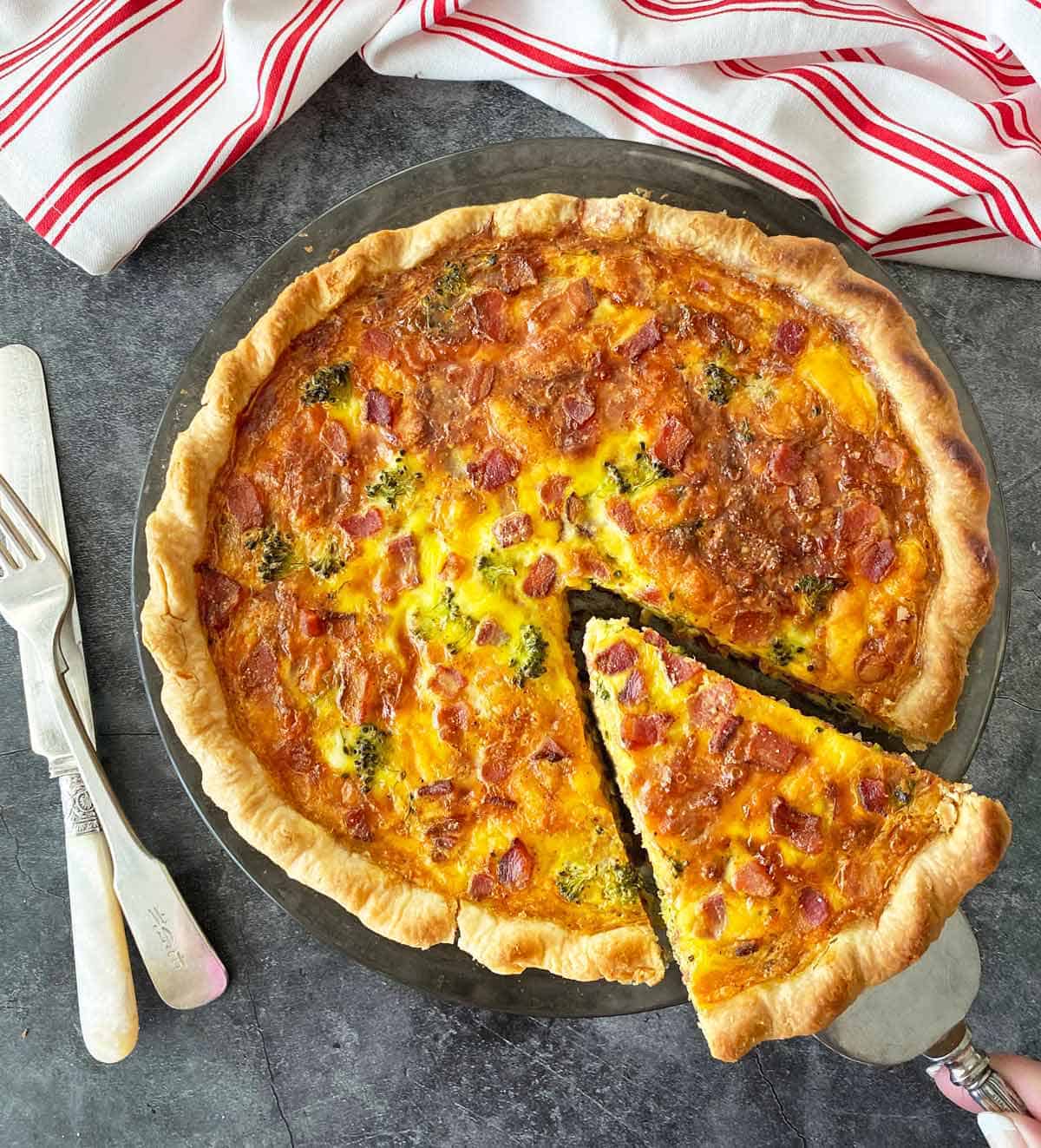 Lifting a slice of broccoli quiche with bacon from the pan to serve.