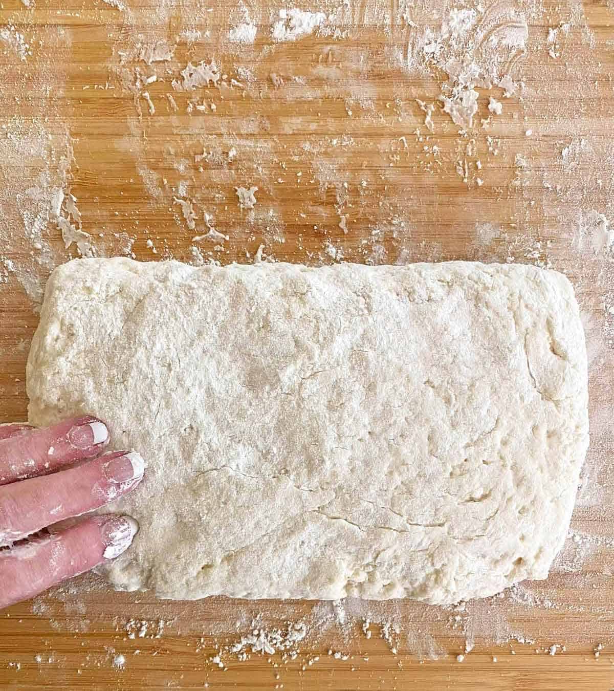 Folding biscuit dough in half from the top to the bottom.