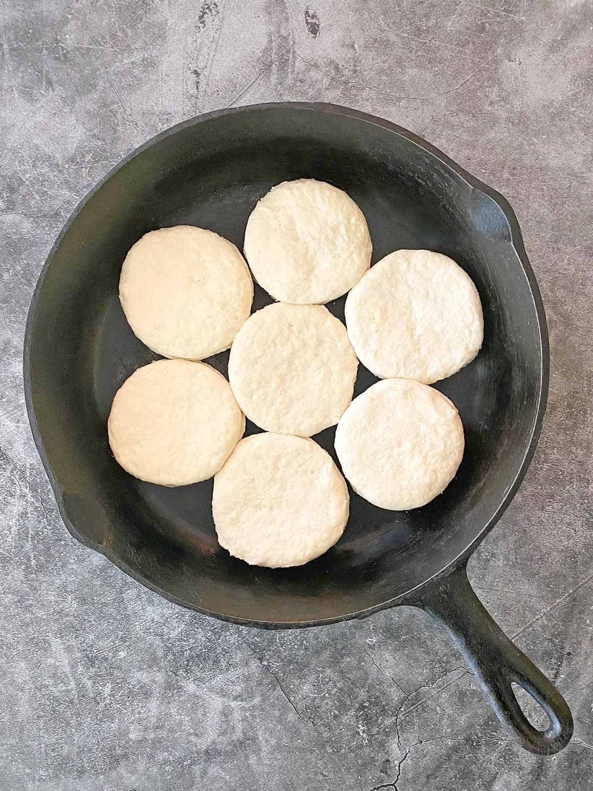 Seven unbaked biscuits in the middle of a cast iron skillet.
