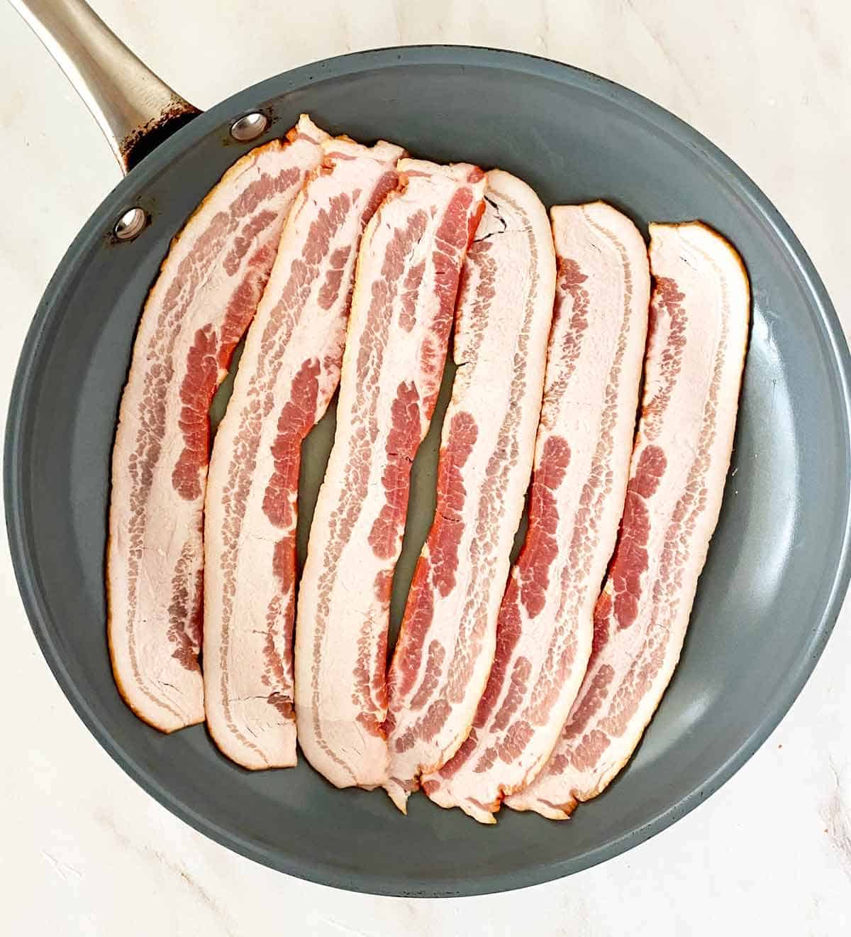 Six raw bacon strips in a nonstick skillet.