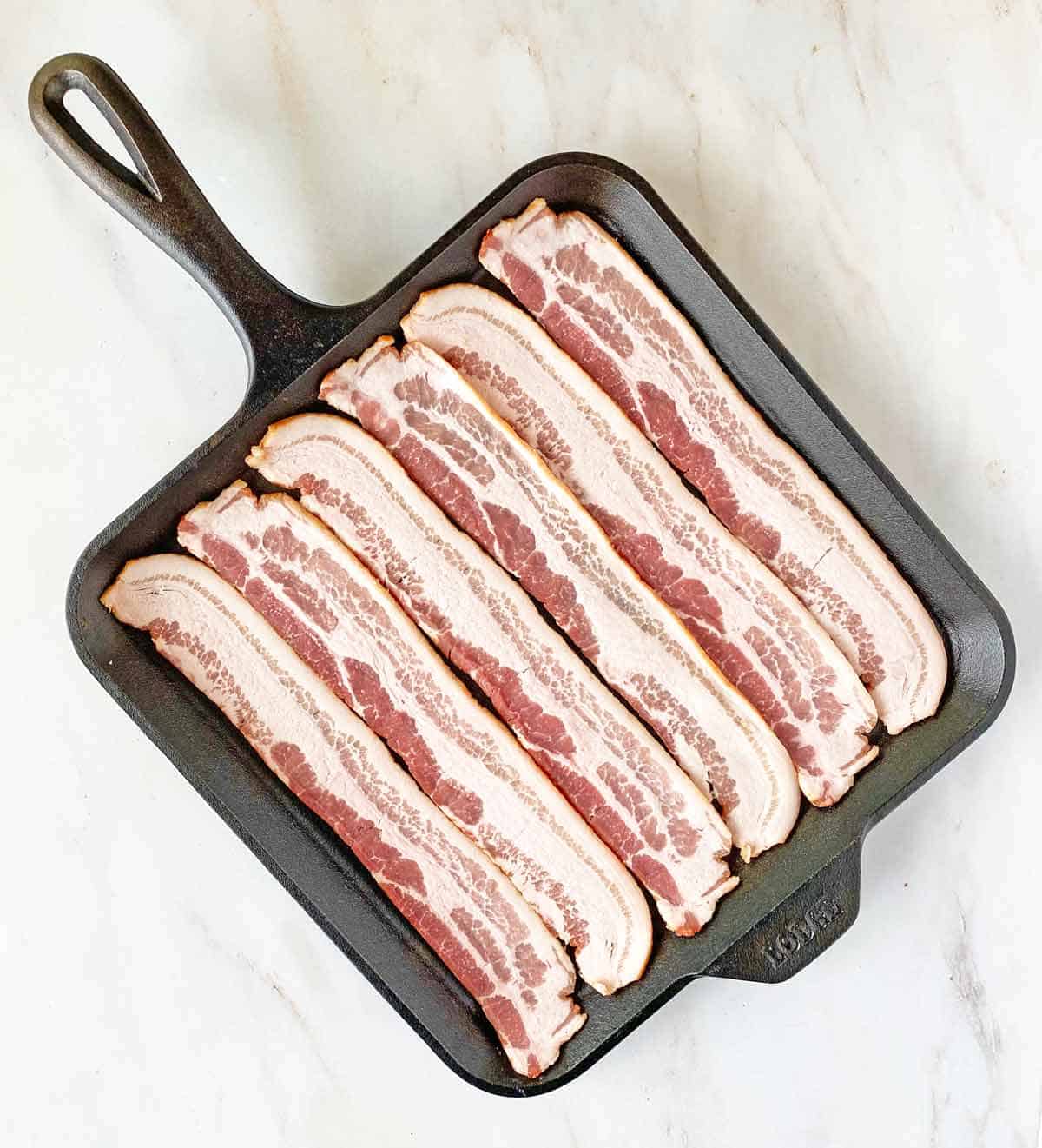 Six bacon slices uncooked in a square cast iron skillet.