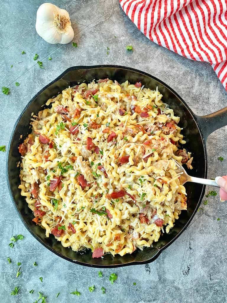 A skillet of hot pasta topped with parmesan cheese cream sauce with chicken and bacon.