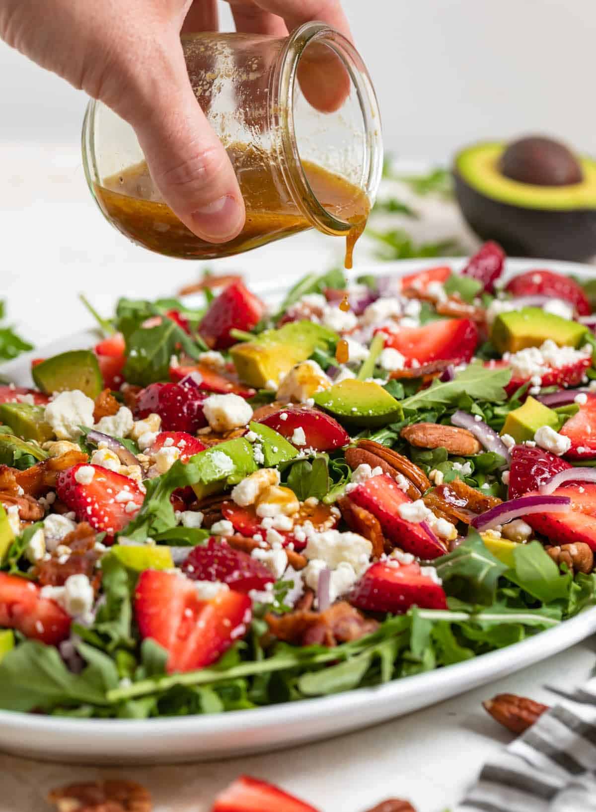 Pouring dressing on a strawberry goat cheese bacon salad.