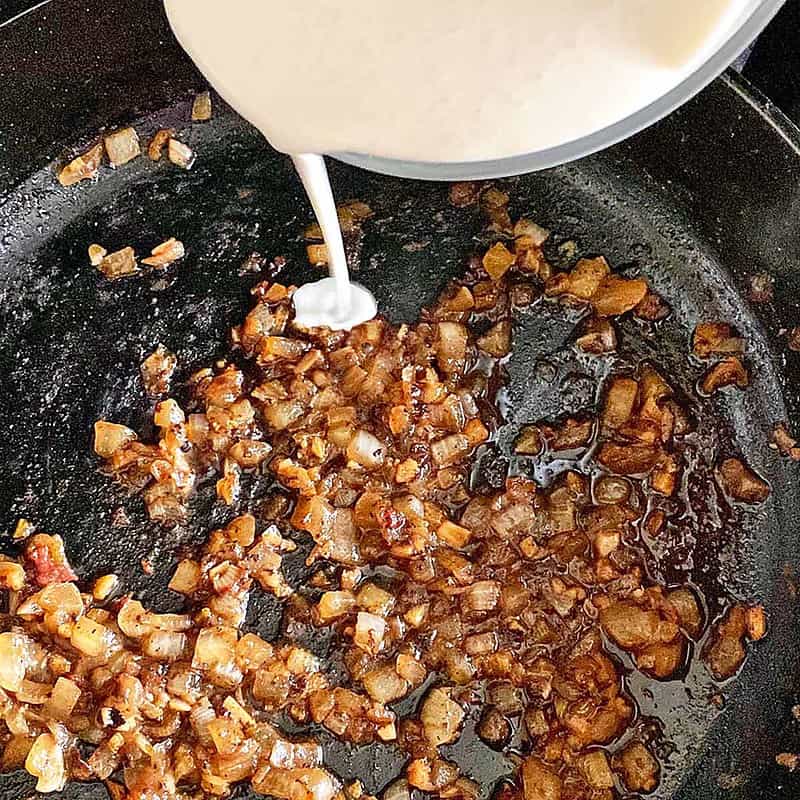 Pouring heavy cream into skillet with caramelized onions to make pasta sauce.
