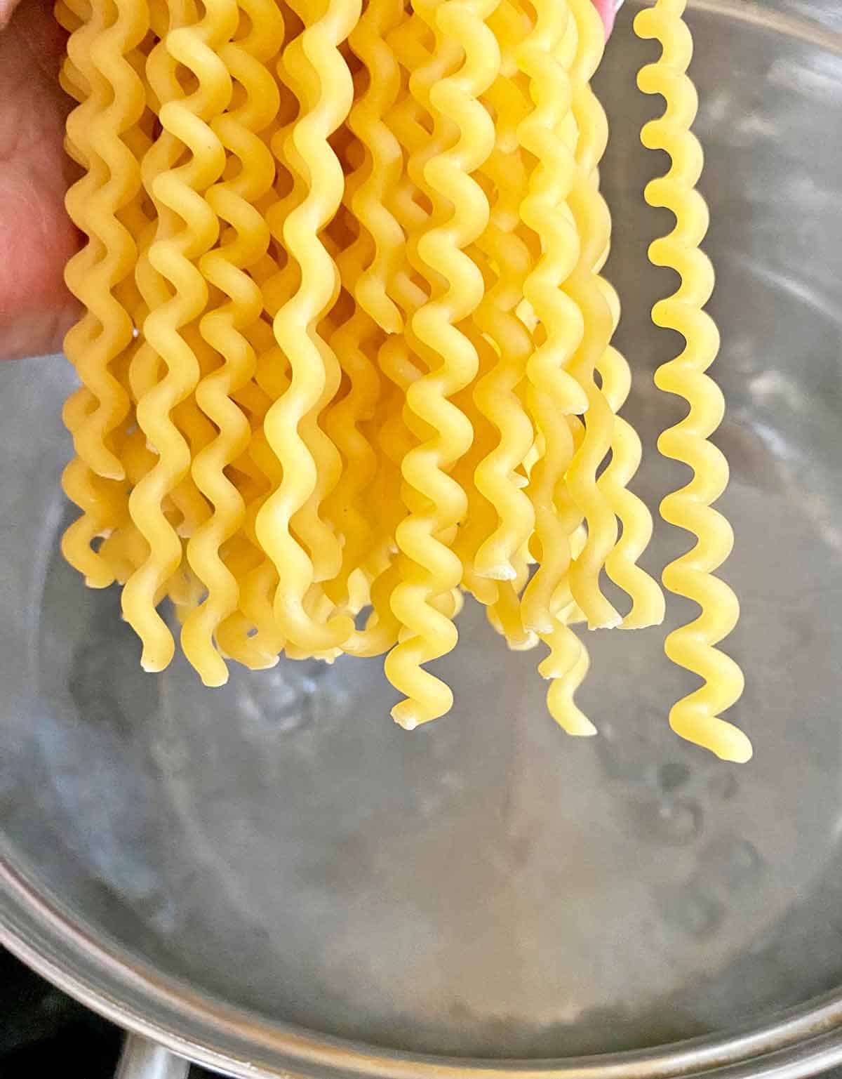 Adding dried pasta noodles to a pot of boiling water.