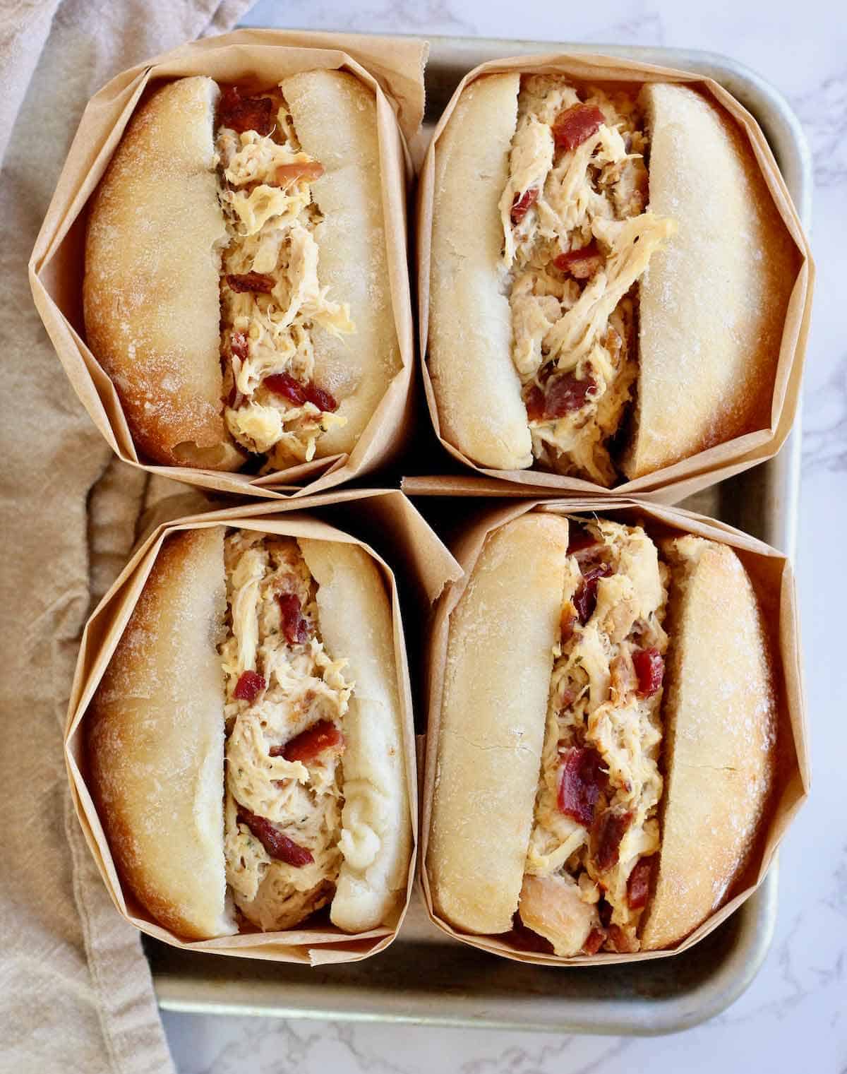 Four chicken bacon sandwiches wrapped in napkins.