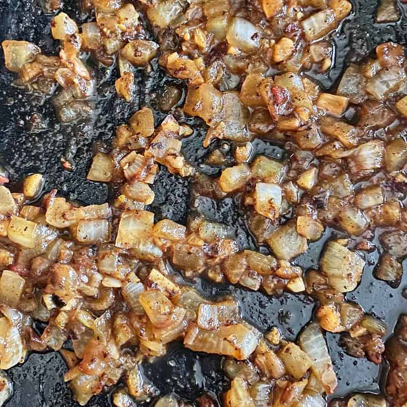Caramelized onions and roasted garlic in a skillet, cooking to reduce liquid.