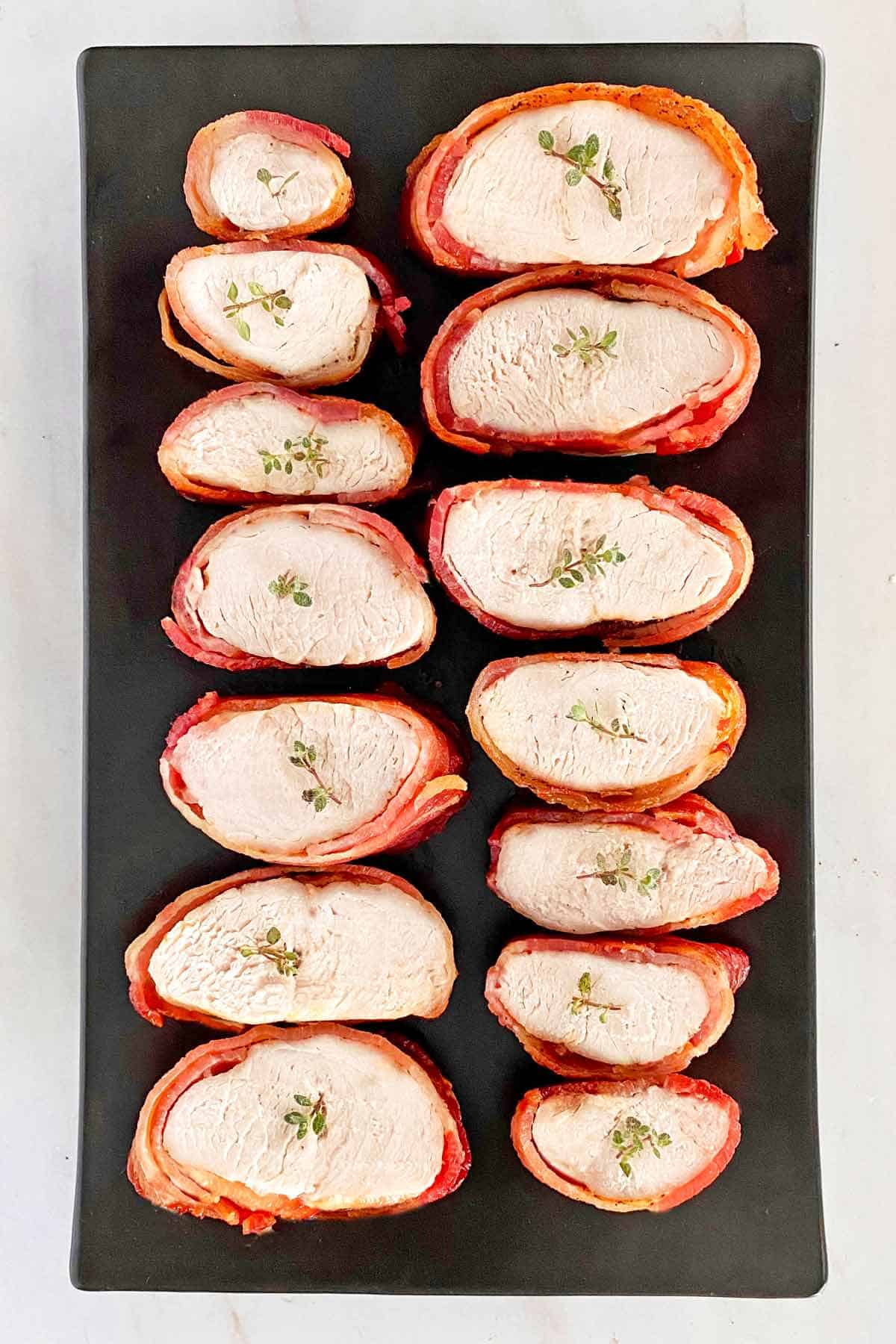 A black platter filled with slices of bacon-wrapped turkey tenderloin.