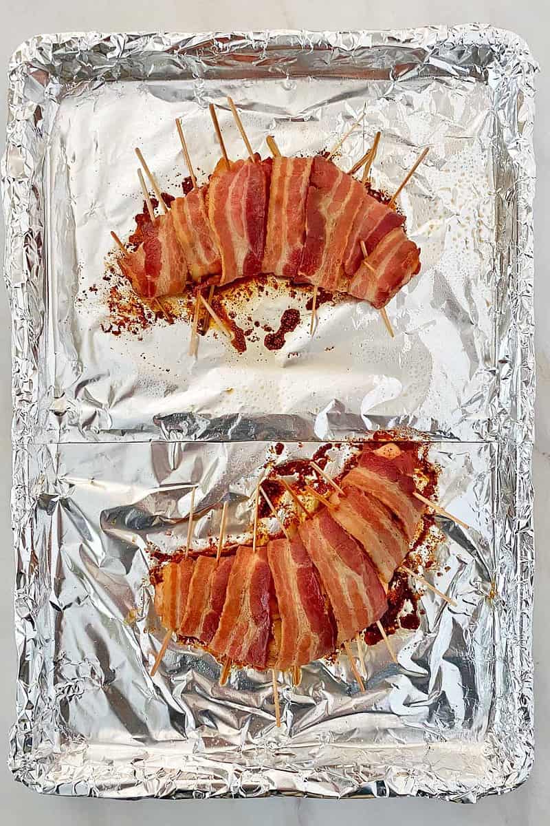 Cooked turkey tenderloins wrapped in bacon on a baking sheet.