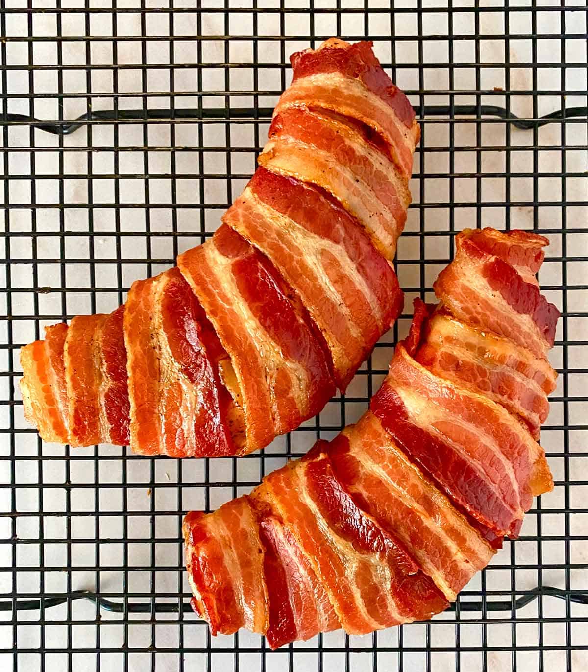 Two cooked turkey tenderloins wrapped in crispy bacon on a cooling rack.