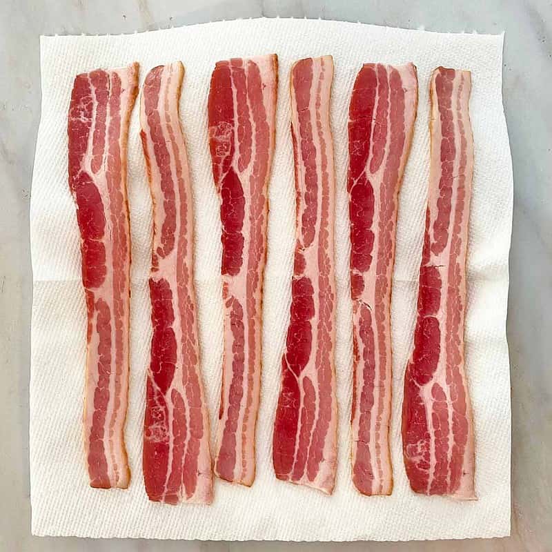 uncooked bacon strips on paper towels.