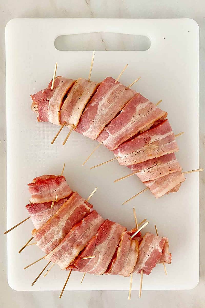 Two turkey tenderloins wrapped in bacon secured with toothpicks.