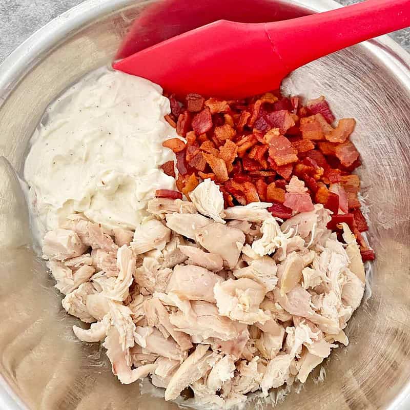 A mixing bowl with chicken, cream cheese and bacon and a red spatula.