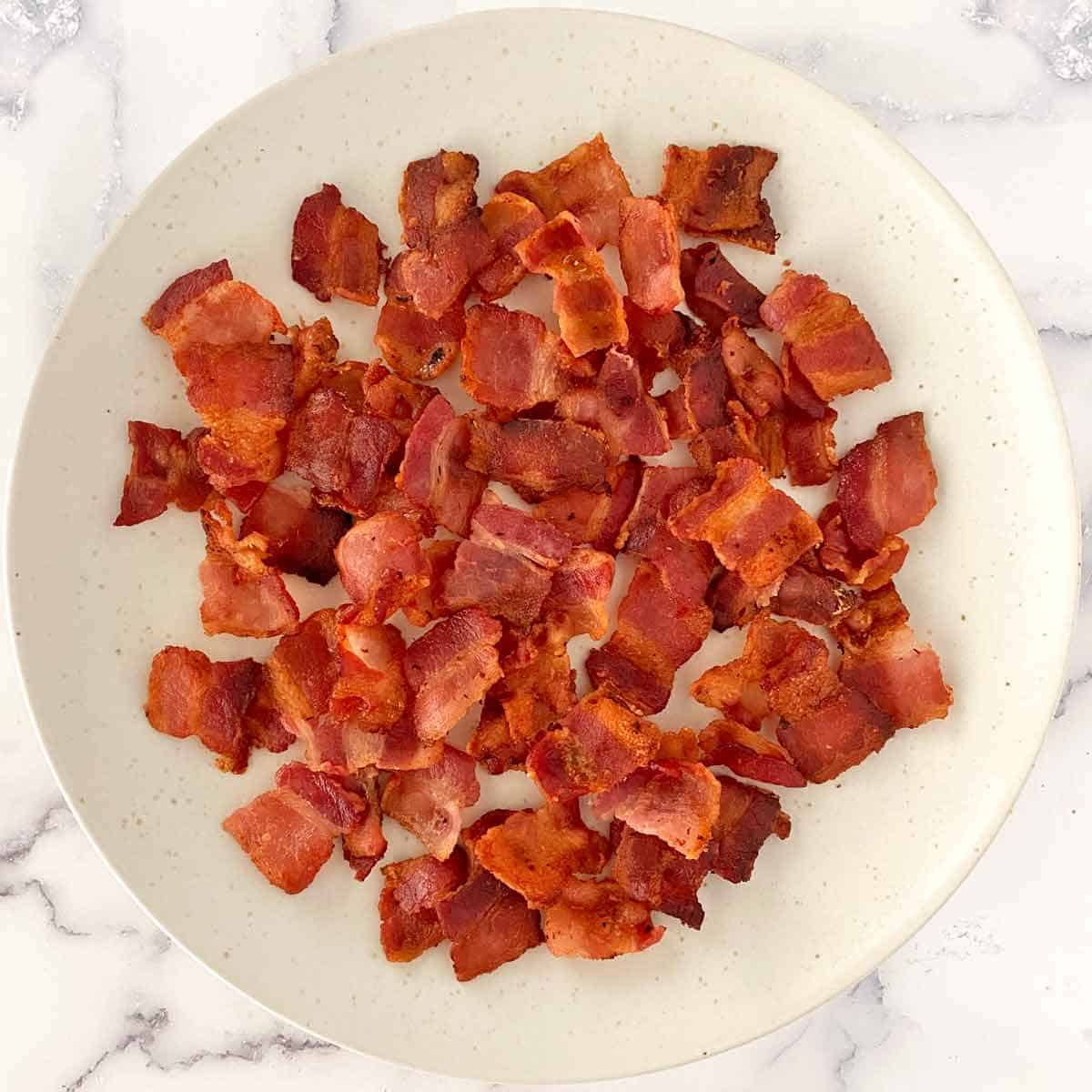 Golden brown chopped cooked bacon on a white plate.