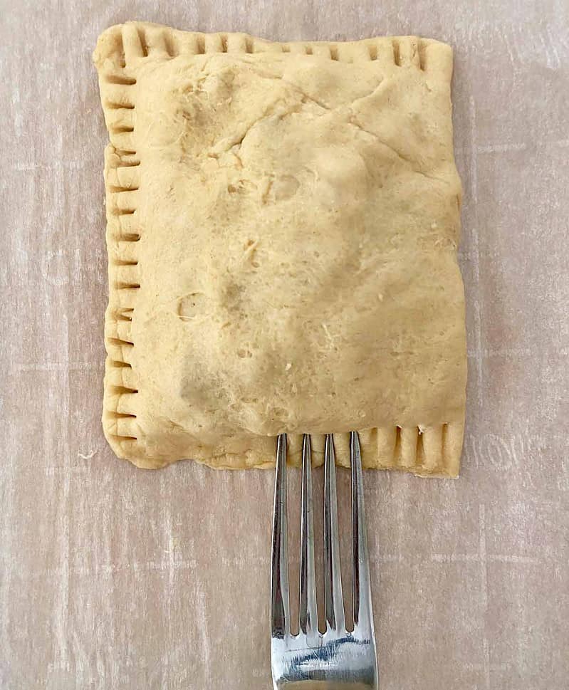 Using a fork to seal the edges of the crescent roll chicken bacon pockets.