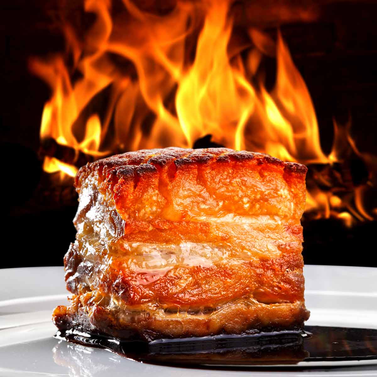 A portion of smoked pork belly in front of a fire.
