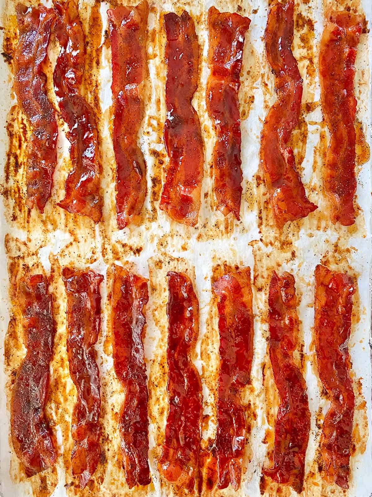 14 strips of honey candied bacon on a parchment lined baking sheet.