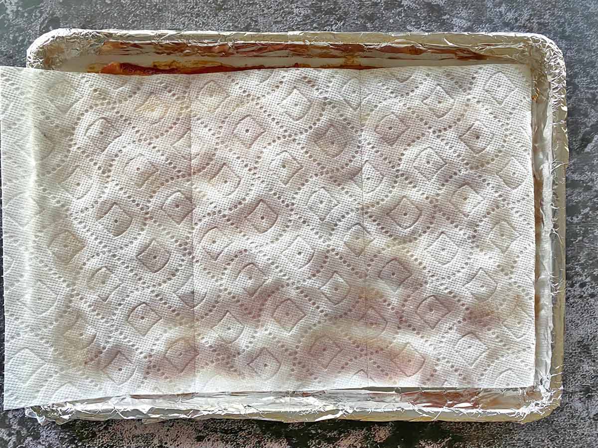 Using paper towels to blot a pan of partially cooked bacon.