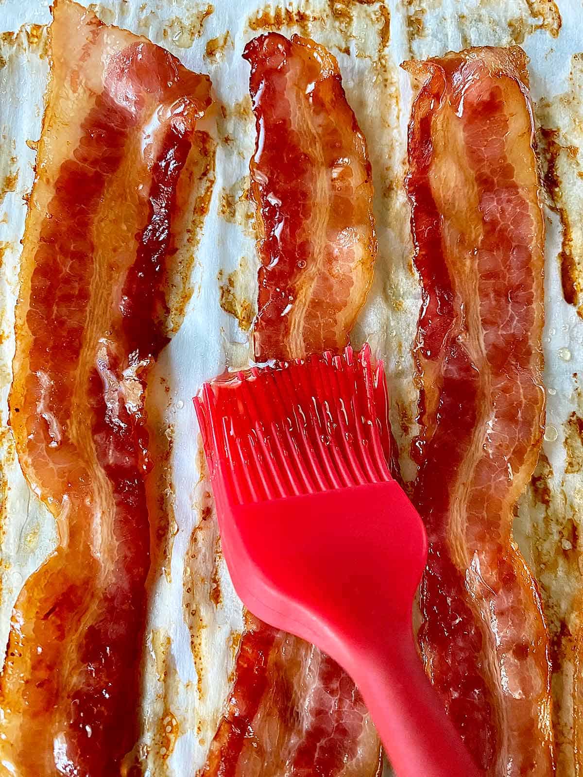 Using a red silicone pastry brush to brush honey glaze on bacon strips.