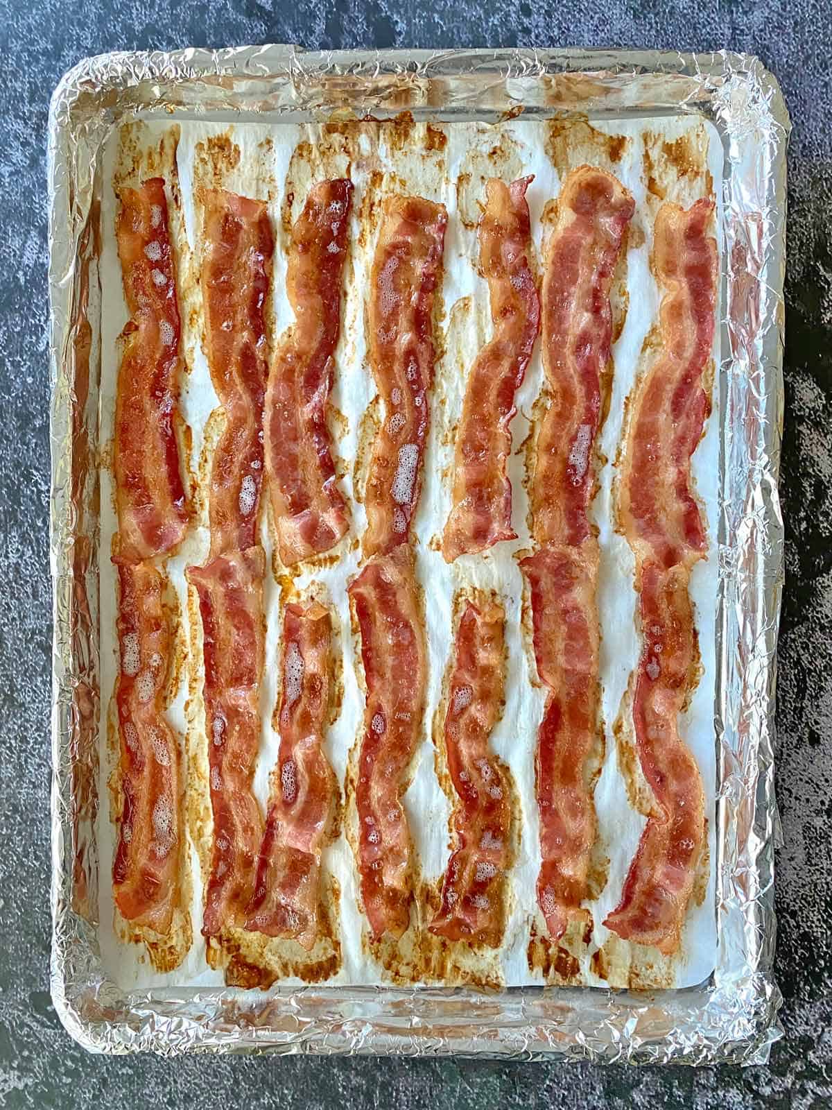 A baking sheet filled with partially cooked bacon strips.