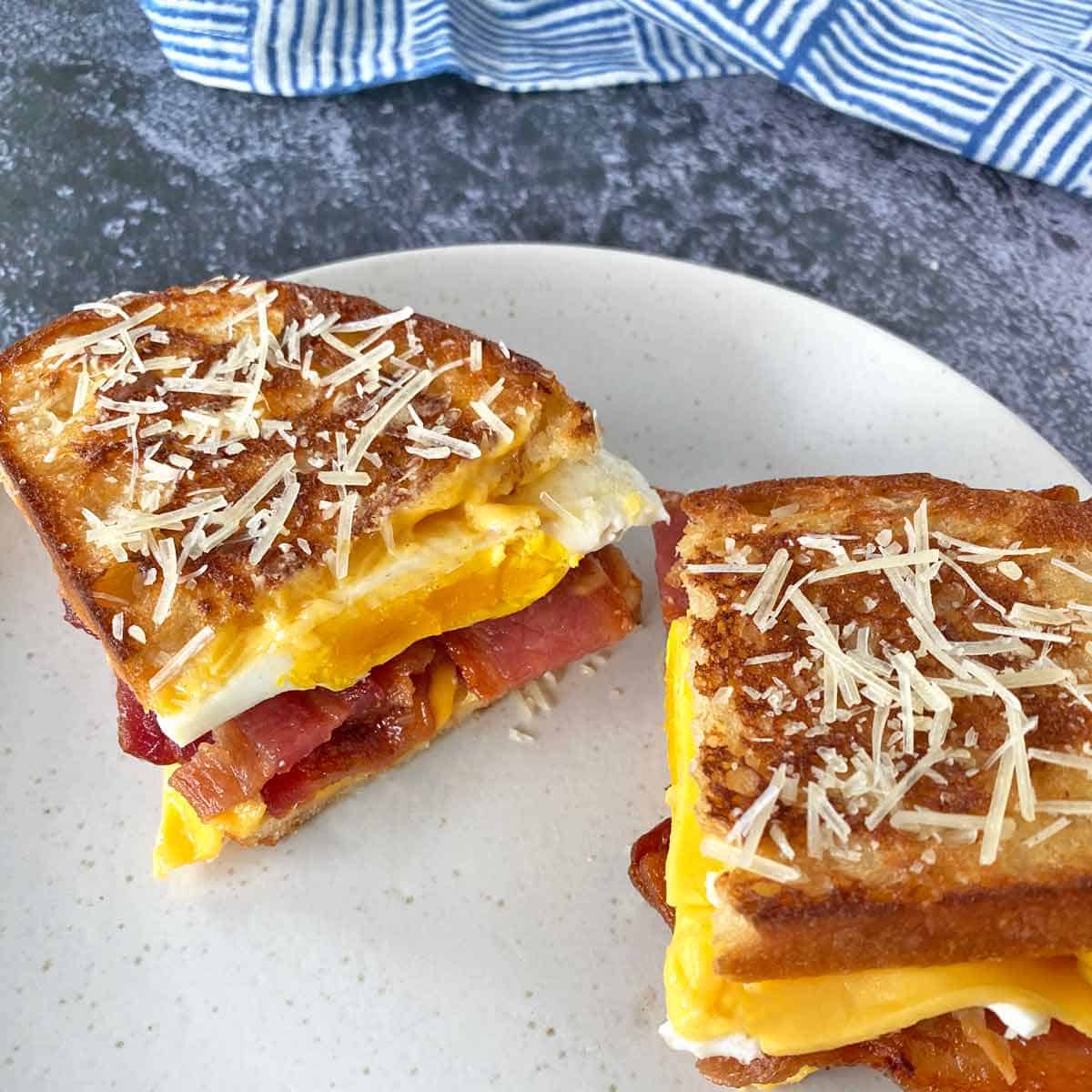 Close up of a bacon breakfast sandwich cut in half on a plate.