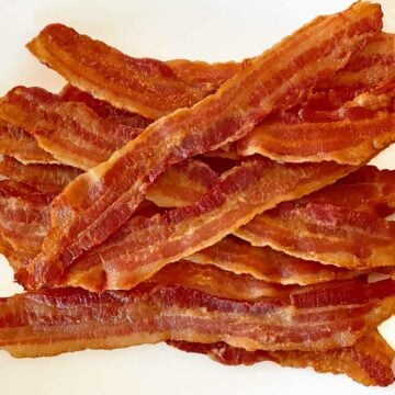 12 slices of crisply cooked bacon on a white plate.