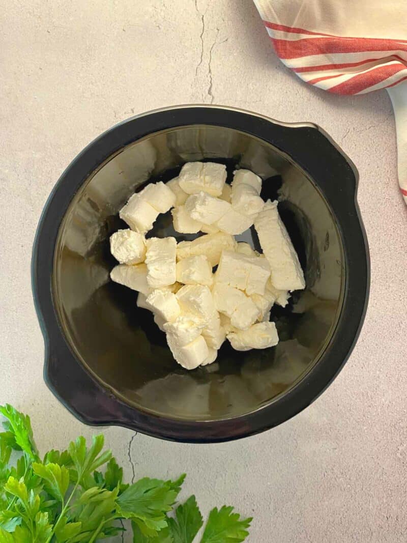 Cubes of cream cheese in the ceramic liner of a slow cooker.