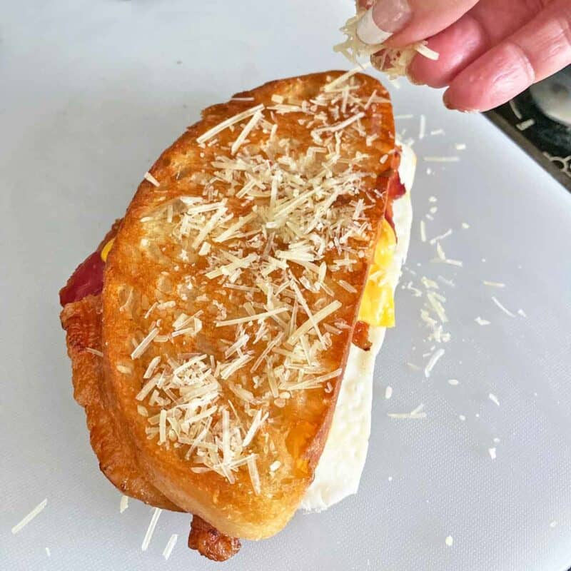 A hand sprinkling shredded cheese on a sandwich.