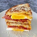 Two halves of a breakfast sandwich stacked to show the layers of bacon, cheese and eggs.
