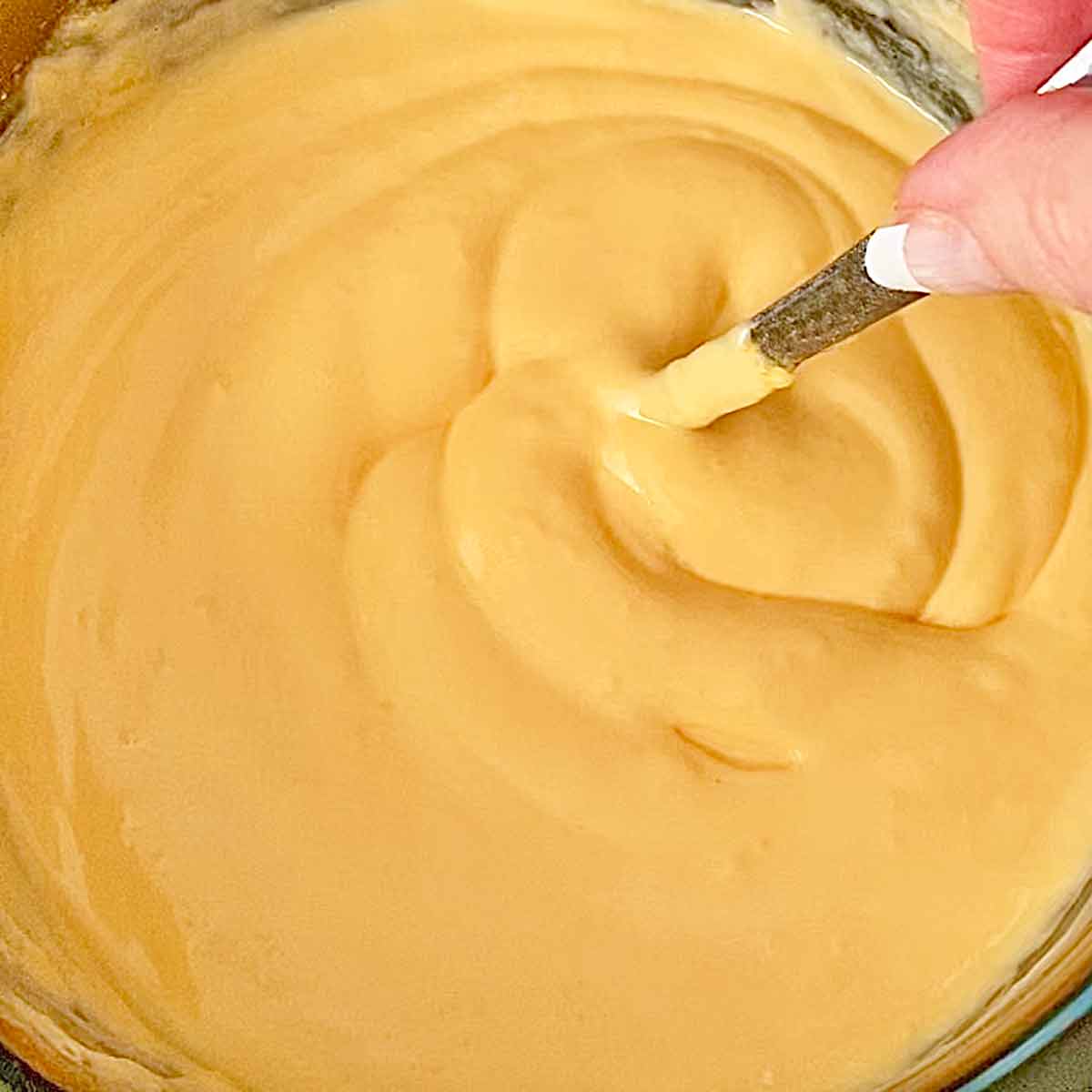 Stirring melted cheeses in a crock pot with a spoon.