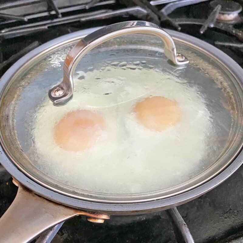 Two basted eggs cooking in a skillet.